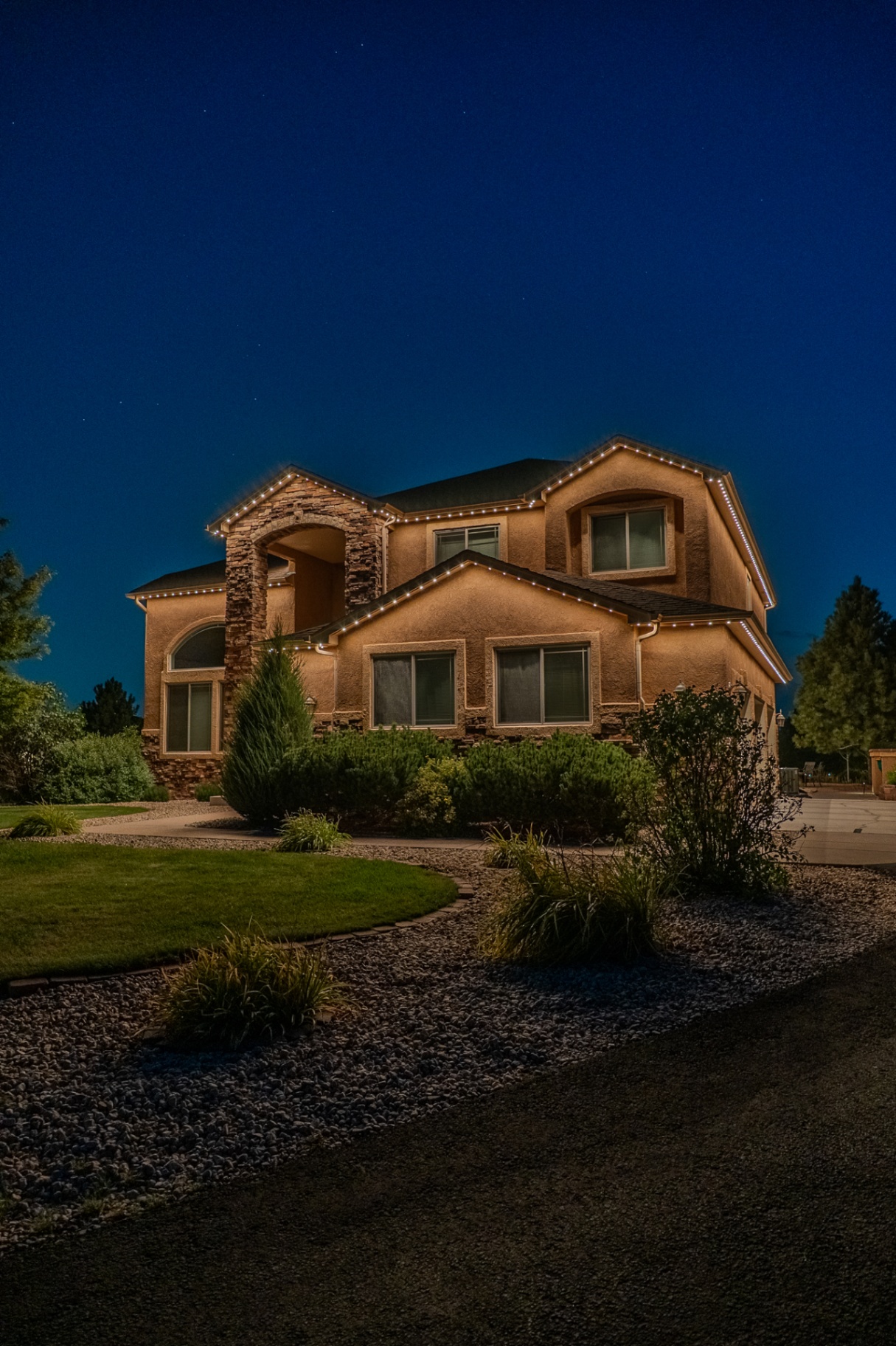 Warm white permanent lighting on a large two-story home at dusk