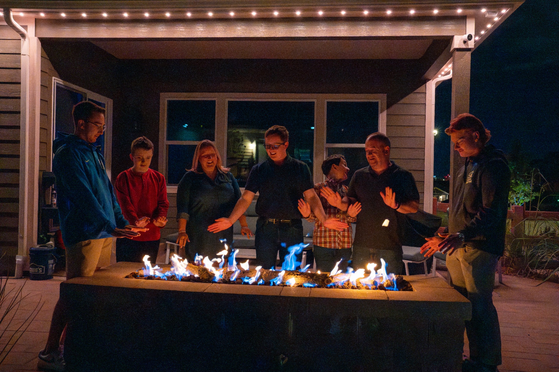 Family gathered by a fire pit under warm white patio lighting